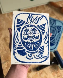 Lino print van een daruma met hojus eromheen