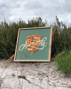 Houten bord met handgeletterde Porsche-typografie en een 3D-geprint Porsche-logo in reliëf