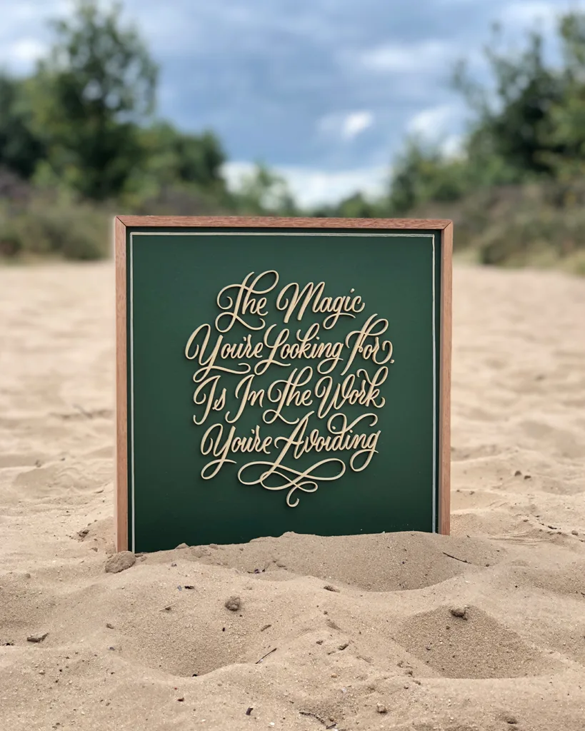 Sierlijke 3D-geprinte kalligrafie met de tekst “The Magic You're Looking For Is In The Work You're Avoiding” op een houten bord met lijst