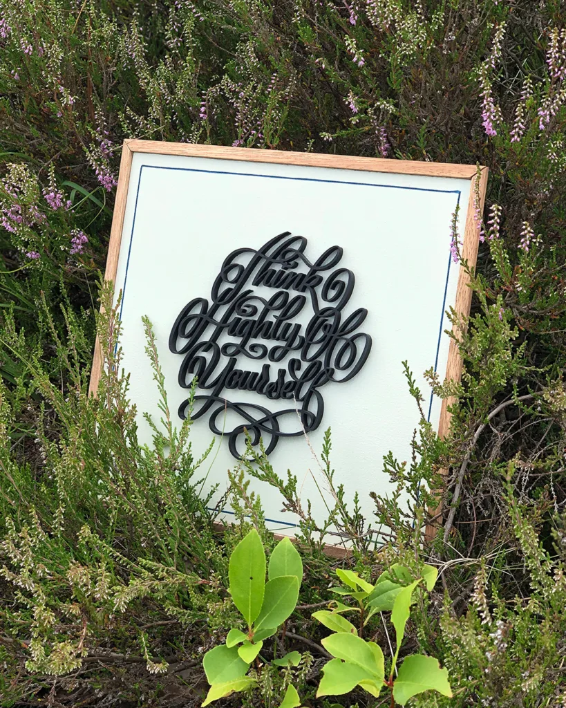 Sierlijke 3D-geprinte kalligrafie in Spencerian Script met de tekst “Think Highly of Yourself” op een houten bord