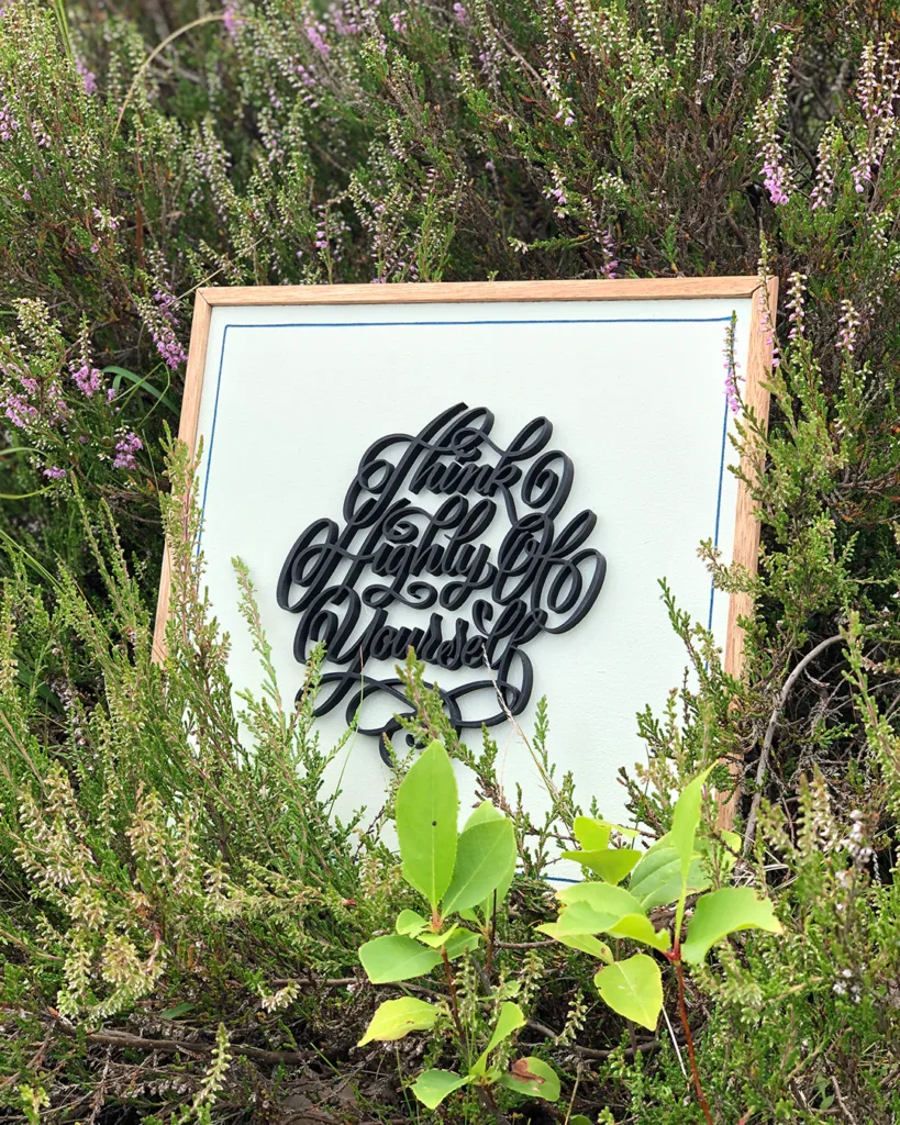 Sierlijke 3D-geprinte kalligrafie in Spencerian Script met de tekst “Think Highly of Yourself” op een houten bord