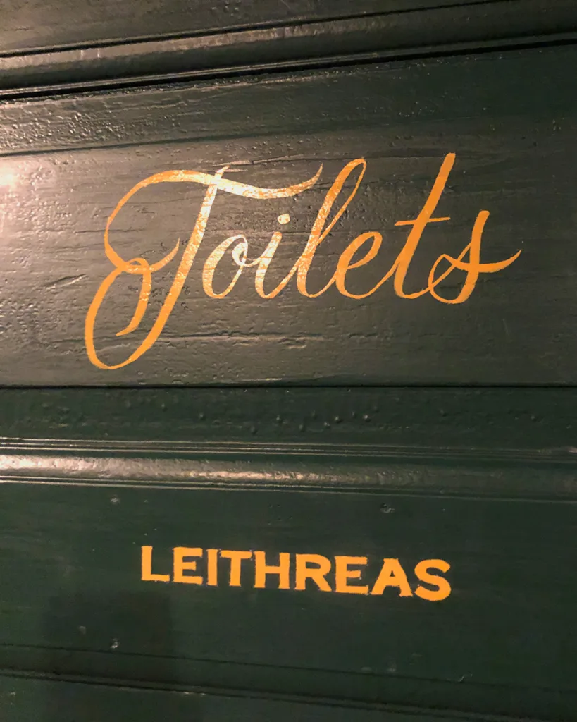 Handgeschilderde gouden scriptbelettering op donkergroene deuren in O' Malley's Irish Pub, uitgevoerd met enamel verf in traditionele signpainting-stijl.