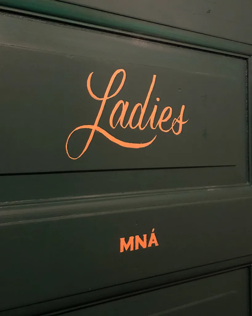 Handgeschilderde gouden scriptbelettering op donkergroene deuren in O' Malley's Irish Pub, uitgevoerd met enamel verf in traditionele signpainting-stijl.