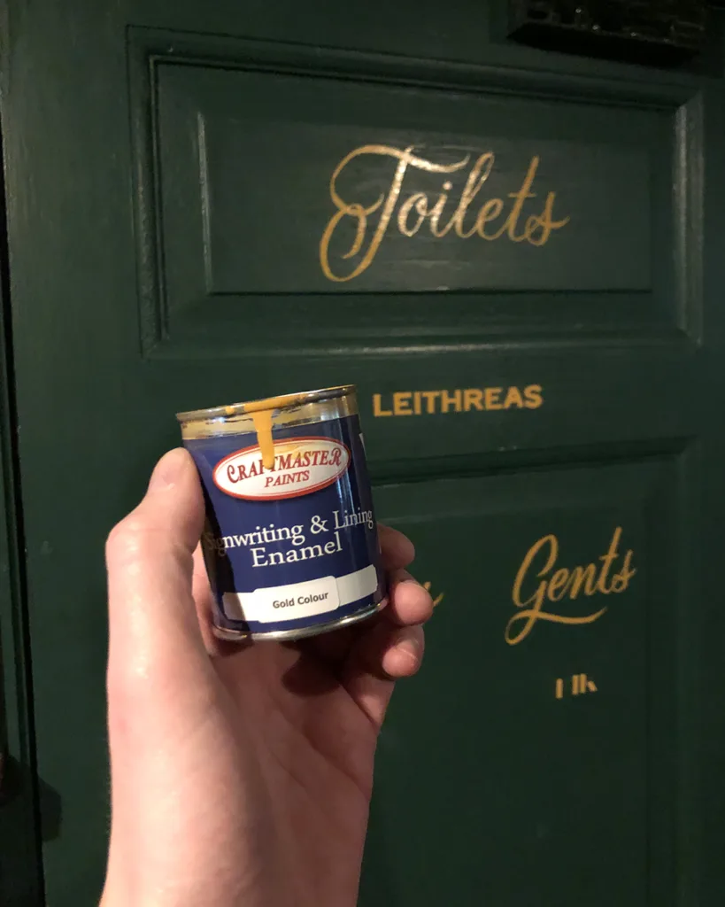 Handgeschilderde gouden scriptbelettering op donkergroene deuren in O' Malley's Irish Pub, uitgevoerd met enamel verf in traditionele signpainting-stijl.