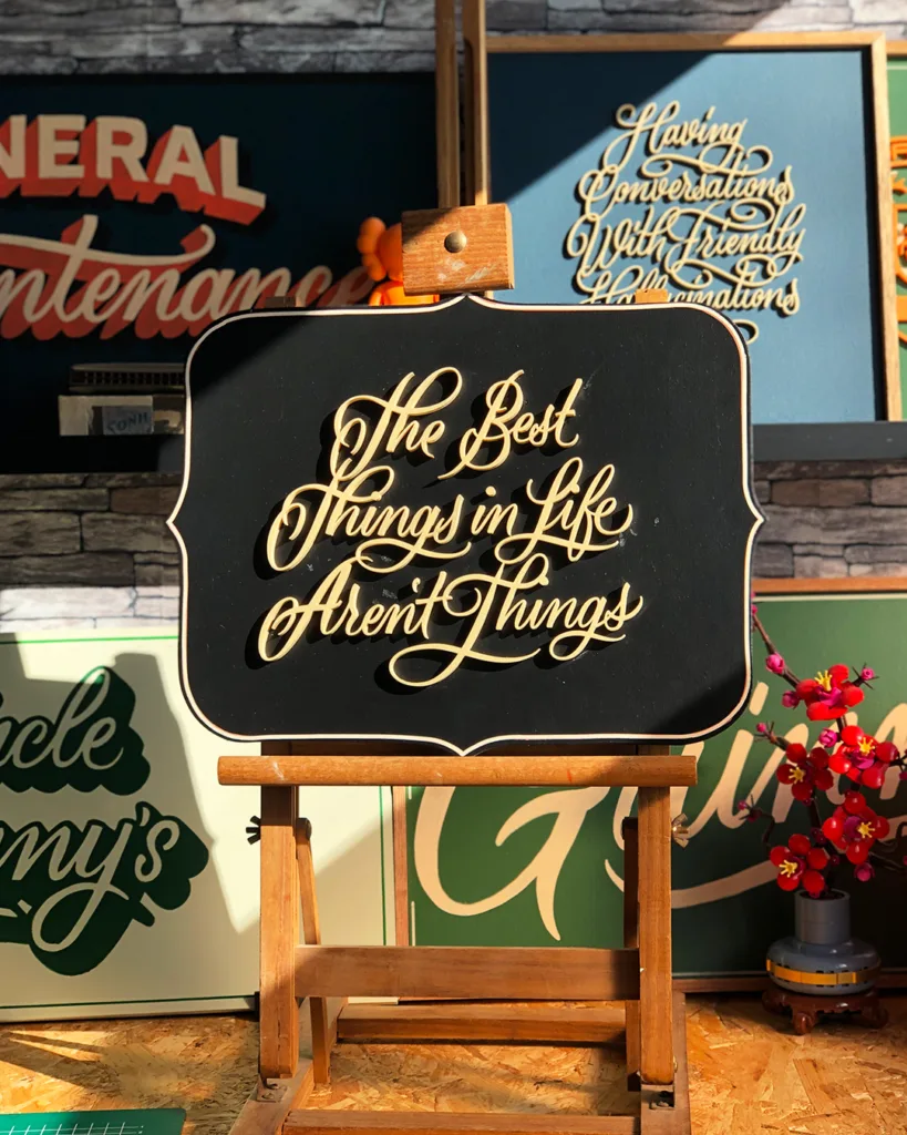 3D-geprinte kalligrafie met de tekst "The Best Things In Life Aren't Things" in beige letters, gemonteerd op een zwart houten bord als onderdeel van de Calligra3D-serie.