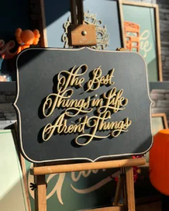3D-geprinte kalligrafie met de tekst "The Best Things In Life Aren't Things" in beige letters, gemonteerd op een zwart houten bord als onderdeel van de Calligra3D-serie.